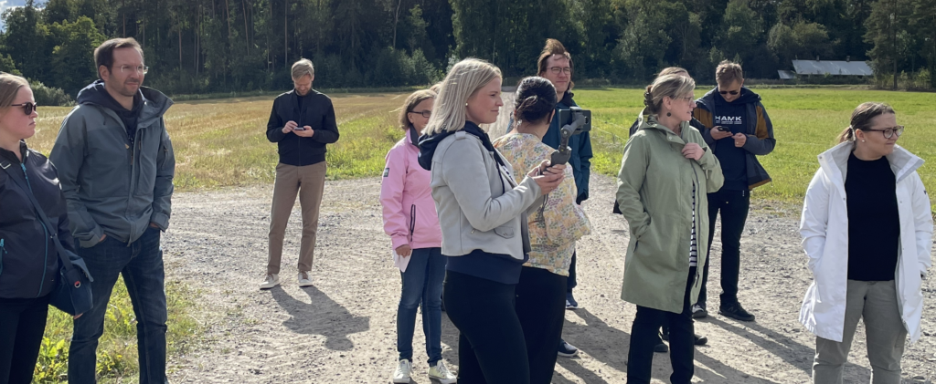 Valokuva hybriditilanteesta. Henkilöitä kampuskierroksella, kierrosta kuvataan puhelimella ja gimbaalilla.